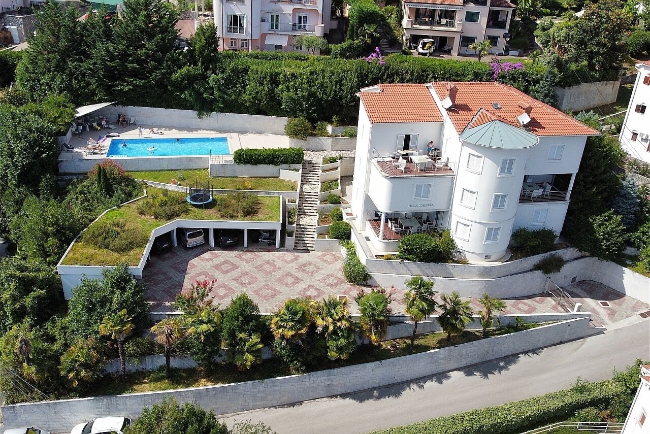 Un edificio de varios pisos con terraza en la azotea, piscina y jardín ajardinado.