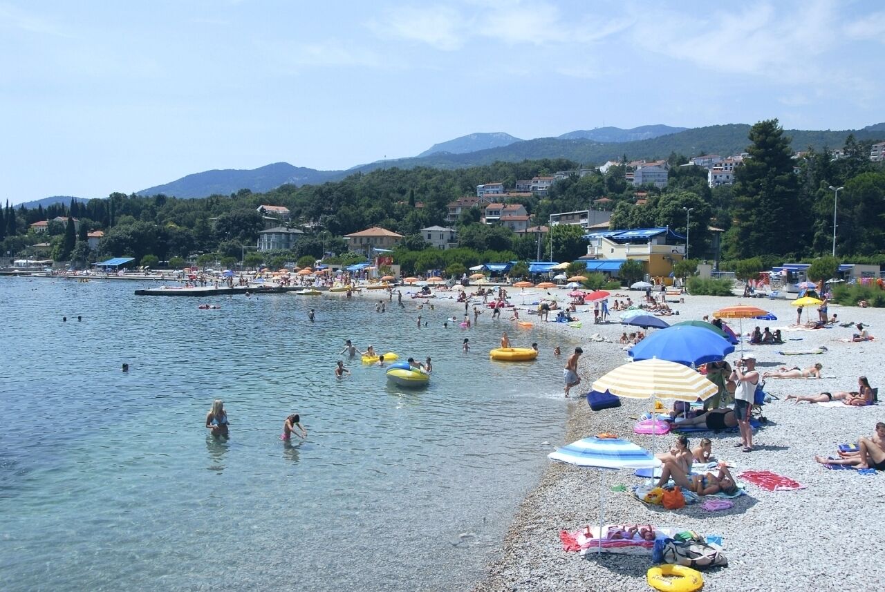 A beach with clear water, people swimming, and colorful umbrellas.