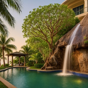 A pool with a waterfall feature, surrounded by lush greenery and palm trees.