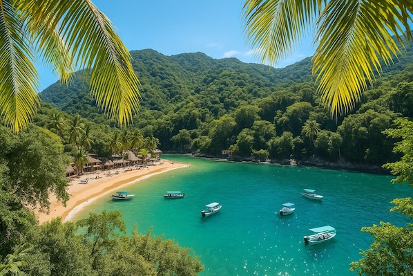 A beach with clear turquoise water, surrounded by lush green hills and palm trees.