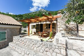 Un bâtiment en pierre avec un toit en tuiles, une pergola en bois, des sièges à l’extérieur et un mur en pierre.