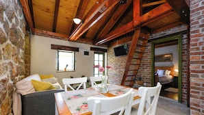 Une pièce chaleureuse avec un plafond en bois, des murs en pierre, une table à manger avec des chaises, un canapé avec des coussins et un téléviseur fixé au mur.