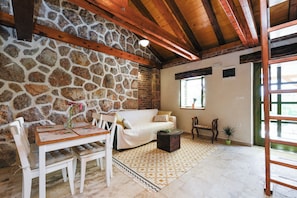 A stone wall, wooden ceiling beams, a white sofa, a wooden dining table with chairs, a coffee table, and a patterned rug. - Traditional Stone House Bura - Nature Park Velebit (Starigrad)