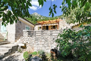 A stone building with a wooden pergola, stone steps, and a view of a mountain. - Traditional Stone House Bura - Nature Park Velebit (Starigrad)