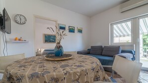 A living room with a round table, a sofa, a TV, and a clock on the wall. - Cozy Apartment in Biograd for Maximum 4 Guests - 3 Minutes Walk to the Beach! (Biograd na Moru)