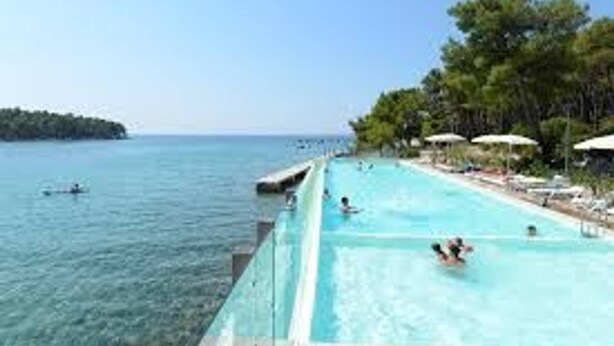 A swimming pool with clear blue water, a view of the sea, and a row of umbrellas along the poolside. - Cozy Apartment in Biograd for Maximum 4 Guests - 3 Minutes Walk to the Beach! (Biograd na Moru)