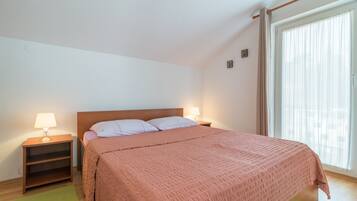 A bedroom with a single bed, two bedside tables with lamps, a green rug, and a window with curtains.