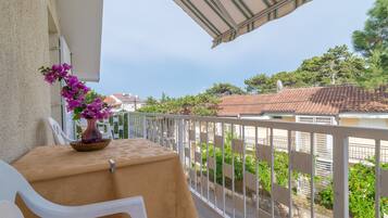 A balcony with a table and chairs, a vase of flowers, and a view of the neighborhood.