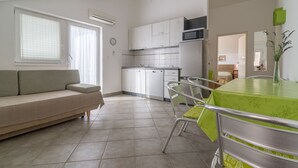Una cocina moderna con armarios blancos, un comedor con una mesa verde y una sala de estar con sofá color crema.