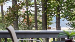 A balcony with a chair and a small table, overlooking a forested area and a body of water. - 🏖️ Peaceful Bayview Studio @ The Shores | Deck + Beach Access + Champagne Welcome ➠ 5693 (Williamsburg)