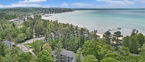 Aerial view of condo buildings and paths among trees beside Grand Traverse Bay.