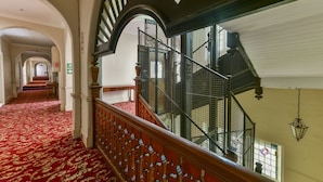 A grand staircase with a red carpet leading to an upper floor, flanked by ornate railings and a view of a hallway with arches. - King Edward Hotel (Port Elizabeth)
