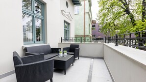Ein Balkon im Freien mit Korbmöbeln, einem kleinen Tisch mit Gläsern und Blick auf ein Gebäude mit rotem Dach.