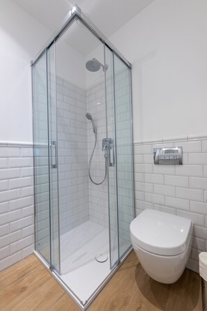 A modern bathroom with a glass-enclosed shower, white tiled walls, and a white toilet.