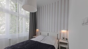 Ein Schlafzimmer mit Bett, Nachttischen, einer Lampe und einem Fenster mit Vorhängen.