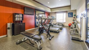 Un gimnasio con cintas de correr, elípticas y una banca para pesas.