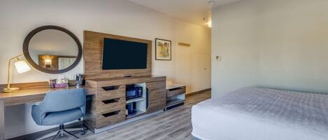 Habitación de hotel con cama, escritorio con silla, televisor y aparador de madera.