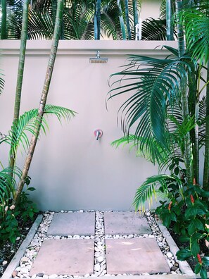 A pathway leading to a wall-mounted shower with a faucet, surrounded by lush greenery and a pebble border. - Perfect 2br Pool Villa In Residence Bangtao Beach4 (Choeng Thale)