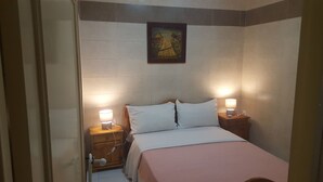 A hotel room with a bed, two bedside lamps, a wooden nightstand, a wall-mounted painting, and a door. - Surfapartment Taghazout Nr 6 (Taghazout)