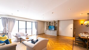 A spacious living room with a large window, a television, and a dining area. - Your Private Oasis Stylish 2br With Spacious Living Room and Pool Access (Bangkok)