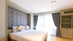 A large bed with a tufted headboard, a wardrobe with a mirror, and a window with curtains. - Your Private Oasis Stylish 2br With Spacious Living Room and Pool Access (Bangkok)
