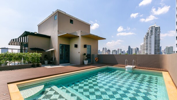 A rooftop swimming pool with a checkered tile pattern, surrounded by a wooden deck and a building with a flat roof. - Your Private Oasis Stylish 2br With Spacious Living Room and Pool Access (Bangkok)
