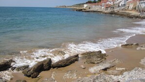 A coastal beach with rocky shoreline and buildings in the background.