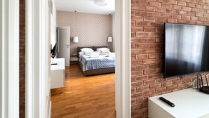 Une chambre d’hôtel avec un mur en briques, un téléviseur à écran plat, un lit recouvert d’une courtepointe matelassée, un bureau avec une lampe et un plancher en bois.