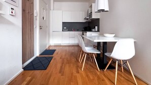 Une cuisine moderne avec des meubles blancs, un plan de travail noir et un coin repas comprenant une table et des chaises blanches.