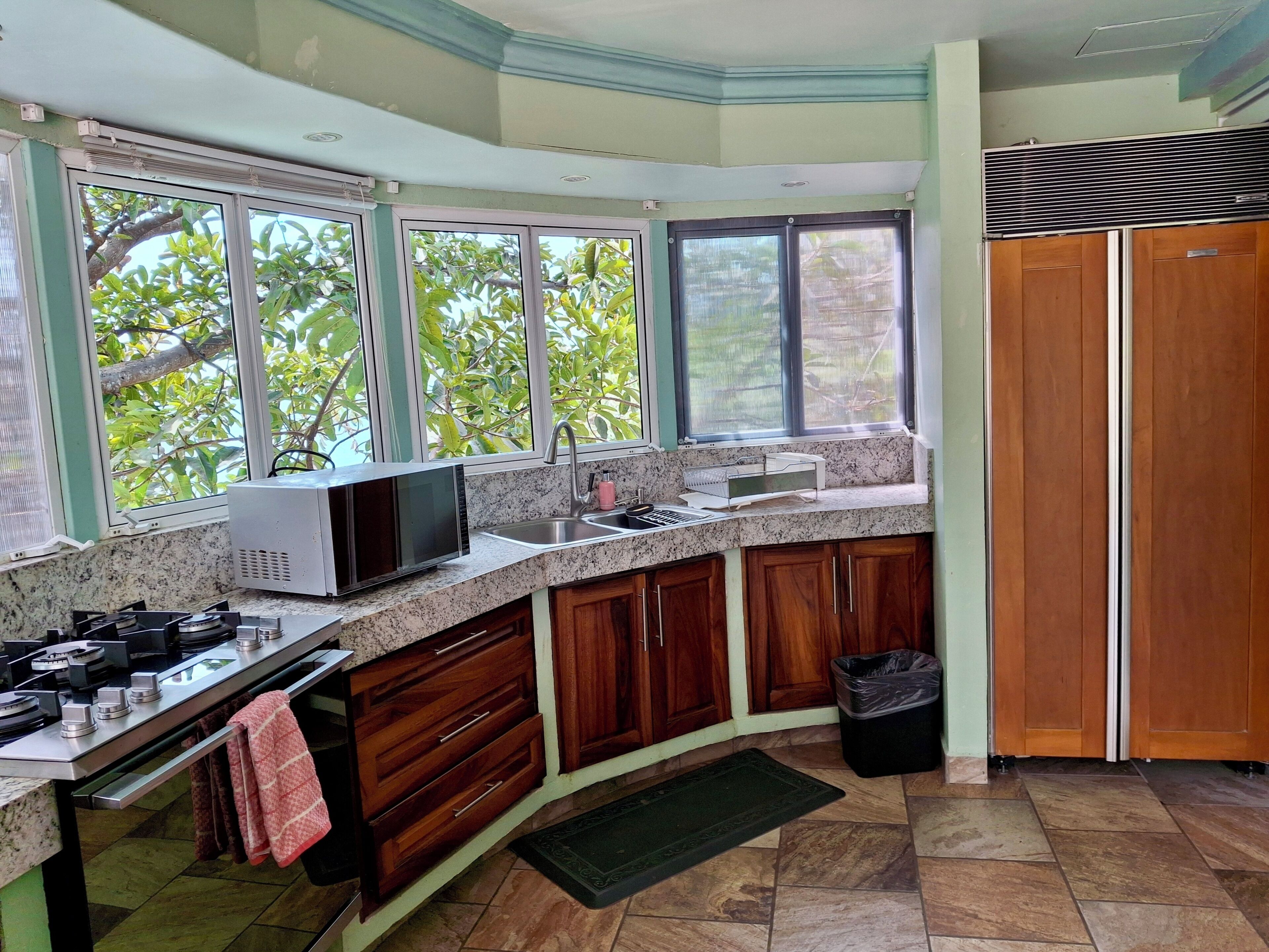 A kitchen with granite countertops, a microwave, a sink, wooden cabinets, and a view of trees through the windows.