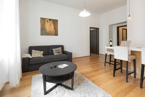 A modern living room with a grey sofa, a black coffee table, a white rug, and a painting on the wall.