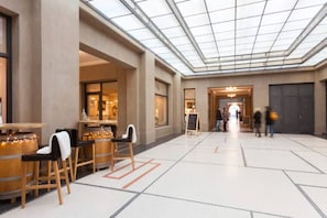 A spacious lobby with a high ceiling and a glass ceiling, wooden furniture, and a central walkway.