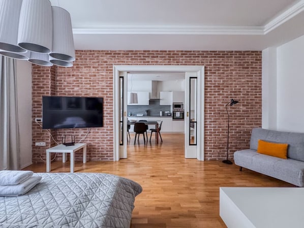 A modern living room with a TV, a sofa, a dining area, and a kitchen in the background.