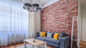 Ein Wohnzimmer mit Ziegelwand, einem grauen Sofa mit gelb-grauen Kissen, einem Holztisch und einer weißen Lehnwand.