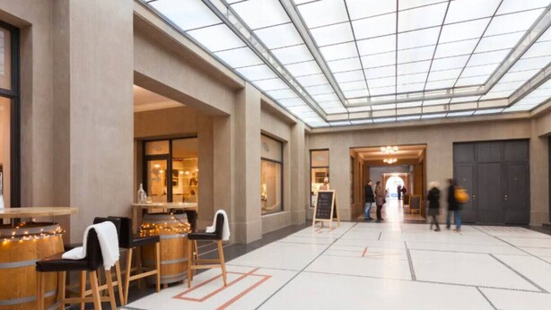 Eine geräumige Lobby mit hoher Decke und Glasdach, Holzmöbeln und einem zentralen Durchgang.