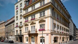 Ein mehrstöckiges Gebäude im klassischen Stil, mit bogenförmigen Fenstern und Balkonen mit Blumenkästen.
