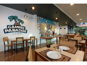 A restaurant with wooden tables and chairs, a mural on the wall, and a sign that reads "Gamers Paradise Camp". - Pool Access Hotel Near Fitness Street soi Ta Iad (Chalong)