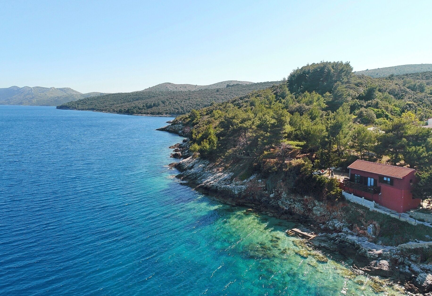 A coastal property with a red building, clear blue waters, and a rocky shoreline.