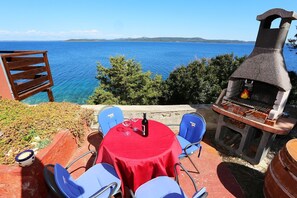 A patio with a table and chairs, a grill, and a view of the sea.