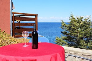A table with a red tablecloth, a wine bottle, and a glass, overlooking a body of water with a wooden structure and greenery in the background.