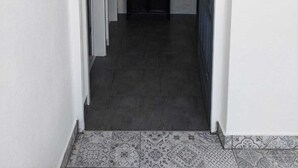 A hallway with a white brick wall, a black cabinet with items on top, and a tiled floor. - Apartment Located Directly on the Sea, With sea Views and Stunning Views (Sali)