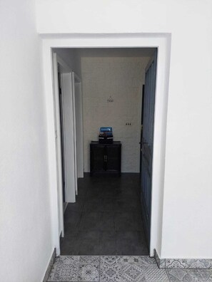 Un pasillo con pared de ladrillo blanco, un mueble negro con objetos encima y piso de baldosas.