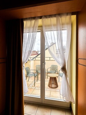 A sliding glass door with white curtains, leading to an outdoor patio with chairs and a table. - Spectacular views guaranteed with A/C! (Prague)
