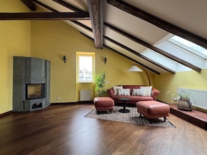 Une pièce aux hauts plafonds avec des poutres apparentes, une cheminée, un canapé et une lucarne.