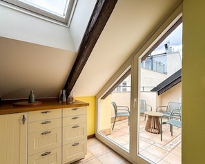 Ein Zimmer mit schrägen Wänden, einer Holztresen, einem weißen Schrank und einer Glastür, die auf eine Außenpatio mit Stühlen und einem Tisch führt.