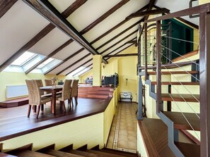 A dining area with a wooden table and chairs, a staircase with metal railings, and a view of the upper floor.