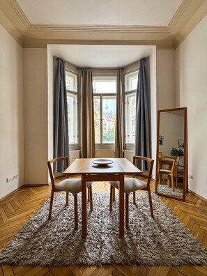 Una stanza con un tavolo da pranzo in legno, quattro sedie, un tappeto soffice, uno specchio grande e una finestra con tende.