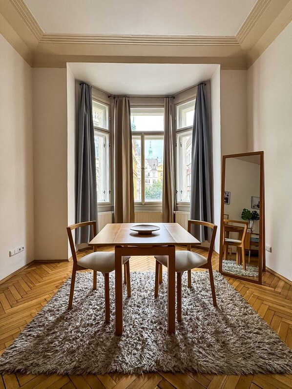 A room with a wooden dining table, four chairs, a fluffy rug, a large mirror, and a window with curtains.