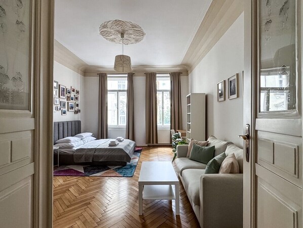 Un dormitorio con cama, mesita de noche, sofá y ventana con cortinas.