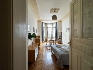 Camera d'albergo con un letto, una scrivania, una sedia, un tavolo, una pianta pensile e una finestra con tende.